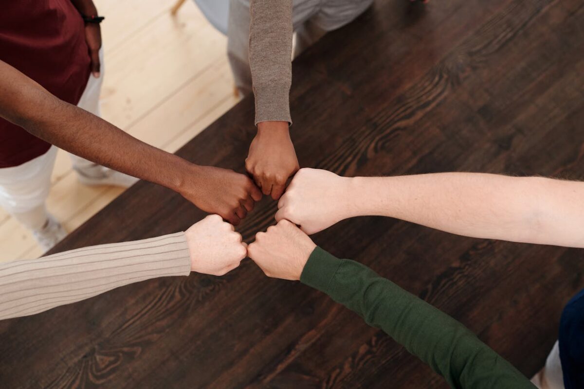 Top view of diverse hands fist bumping on wooden table, symbolizing teamwork, unity, and cooperation.